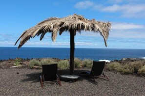 Une scène de plage avec un parasol en chaume, deux chaises et une vue sur l’océan.