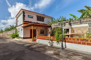 Uma casa de dois andares com telhado de telhas, varanda e um pequeno jardim.