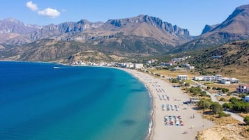 Una playa costera con mar azul cristalino, arena dorada y montañas al fondo.