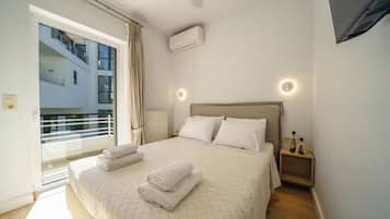 Un dormitorio con cama, almohadas, mesita de noche, aire acondicionado instalado en la pared y ventana con cortinas.