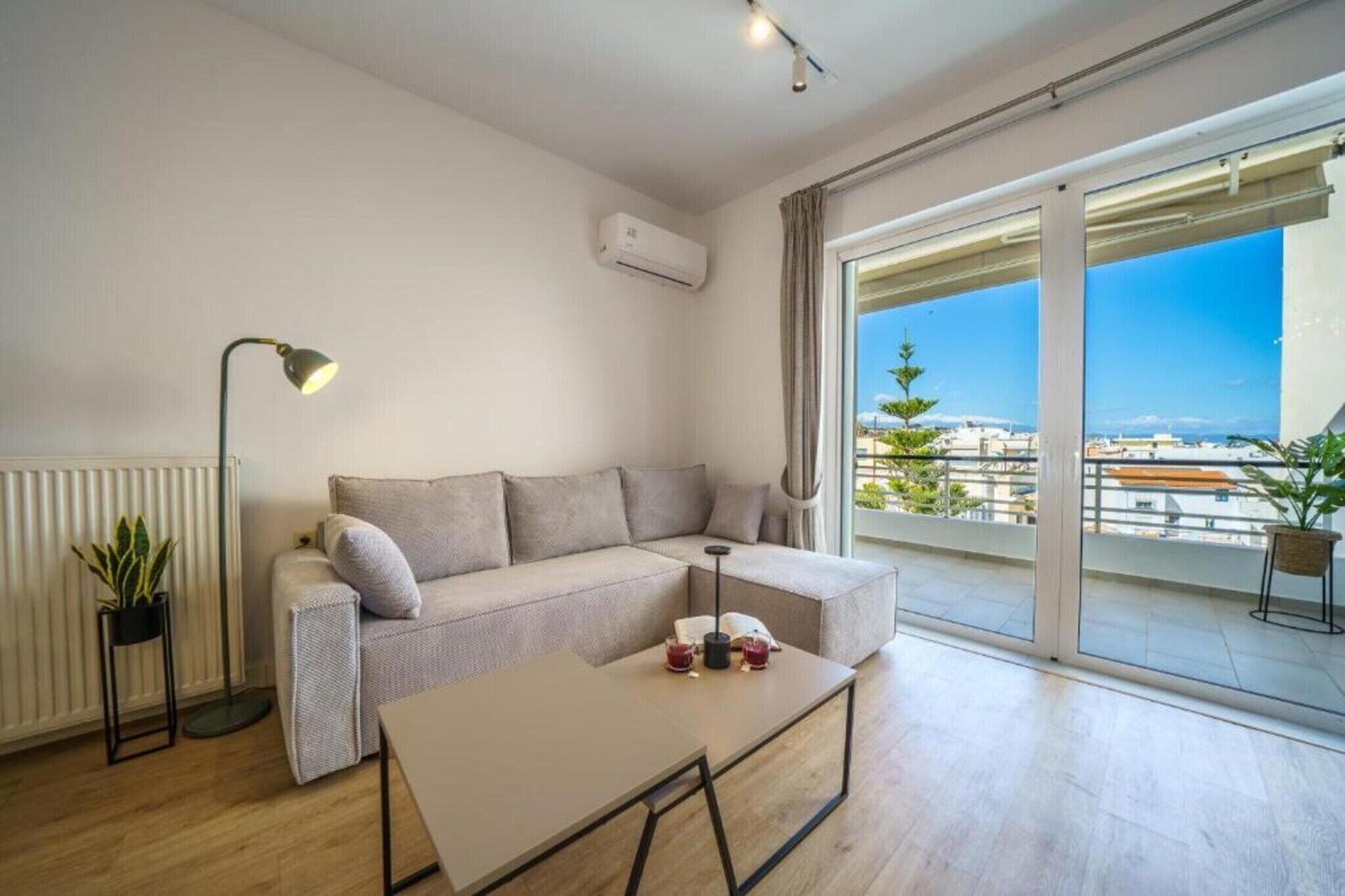 Una sala moderna con un sofá, una mesa de centro, una lámpara de pie y vistas de la ciudad a través de amplios ventanales.