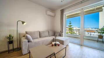 Una sala moderna con un sofá, una mesa de centro, una lámpara de pie y vistas de la ciudad a través de amplios ventanales.