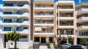 Un edificio residencial de varios pisos con balcones, una entrada con portón y automóviles estacionados.