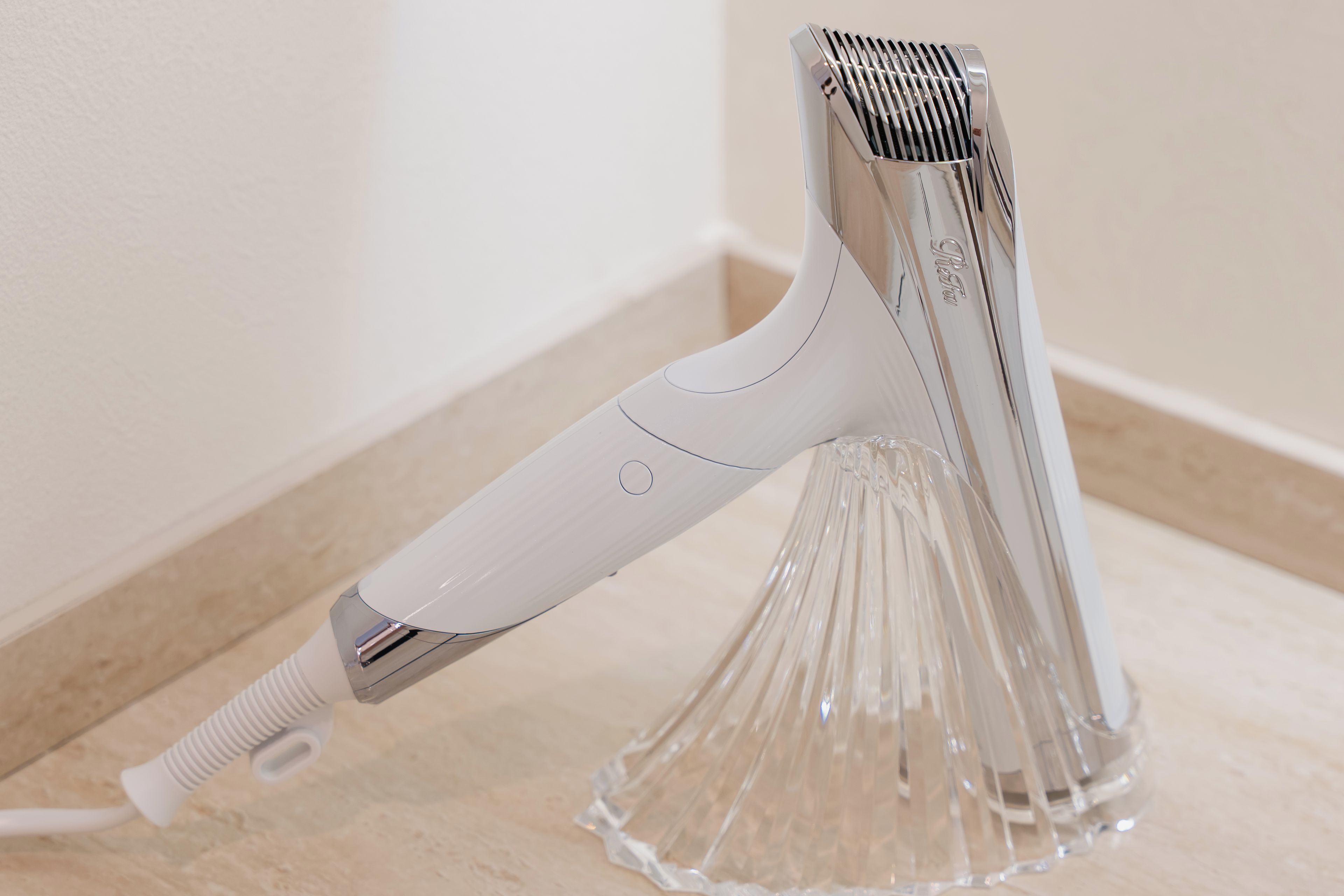 A hair clipper with a white handle and metallic blades, placed on a clear glass stand.