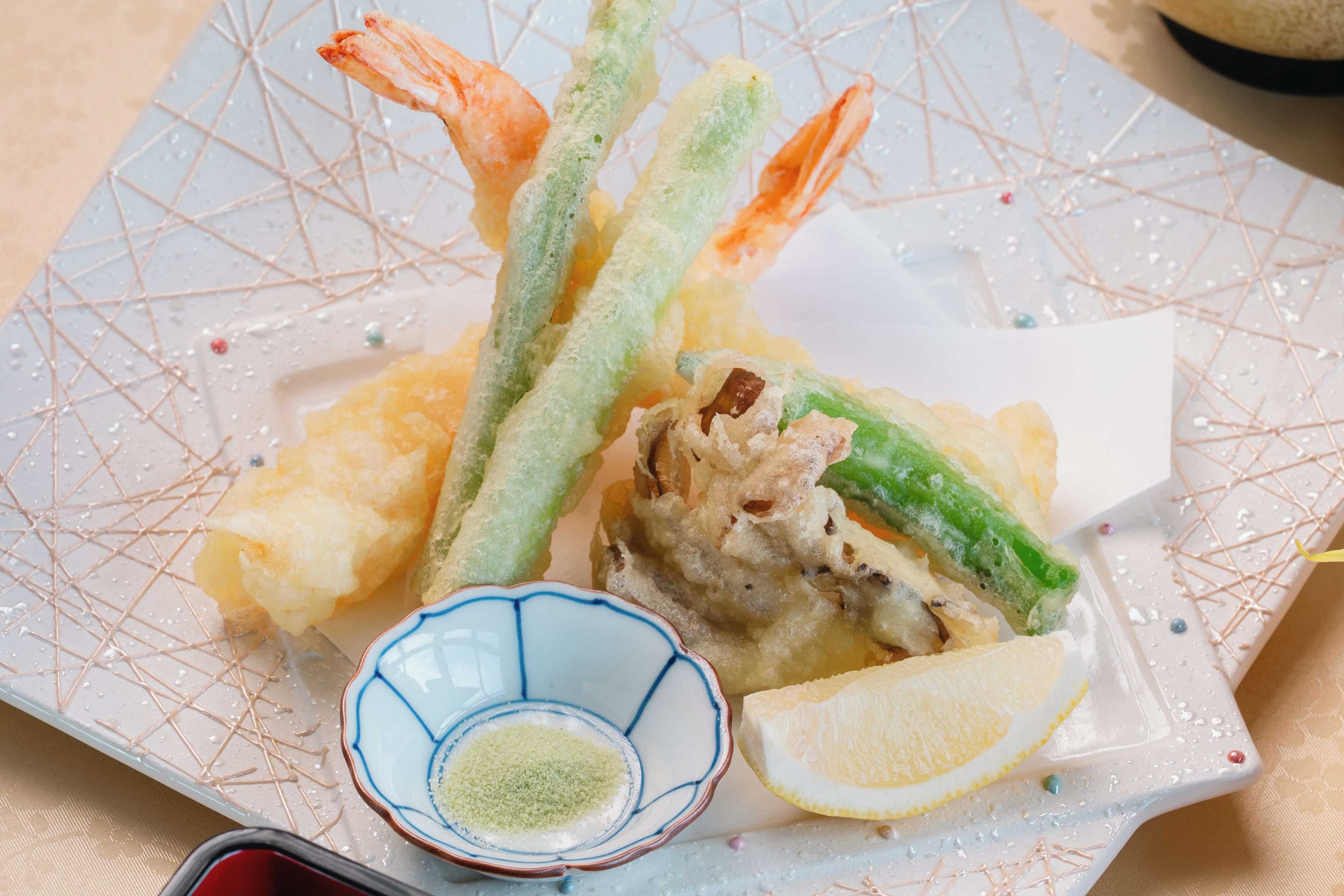 A plate of tempura with shrimp and vegetables, a lemon wedge, and a small bowl of green dipping sauce.