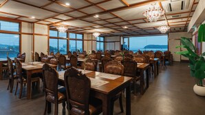 A spacious dining area with wooden tables and chairs, large windows, and a view of the sea. - Fleurs Resort & Hotel (Nishio)