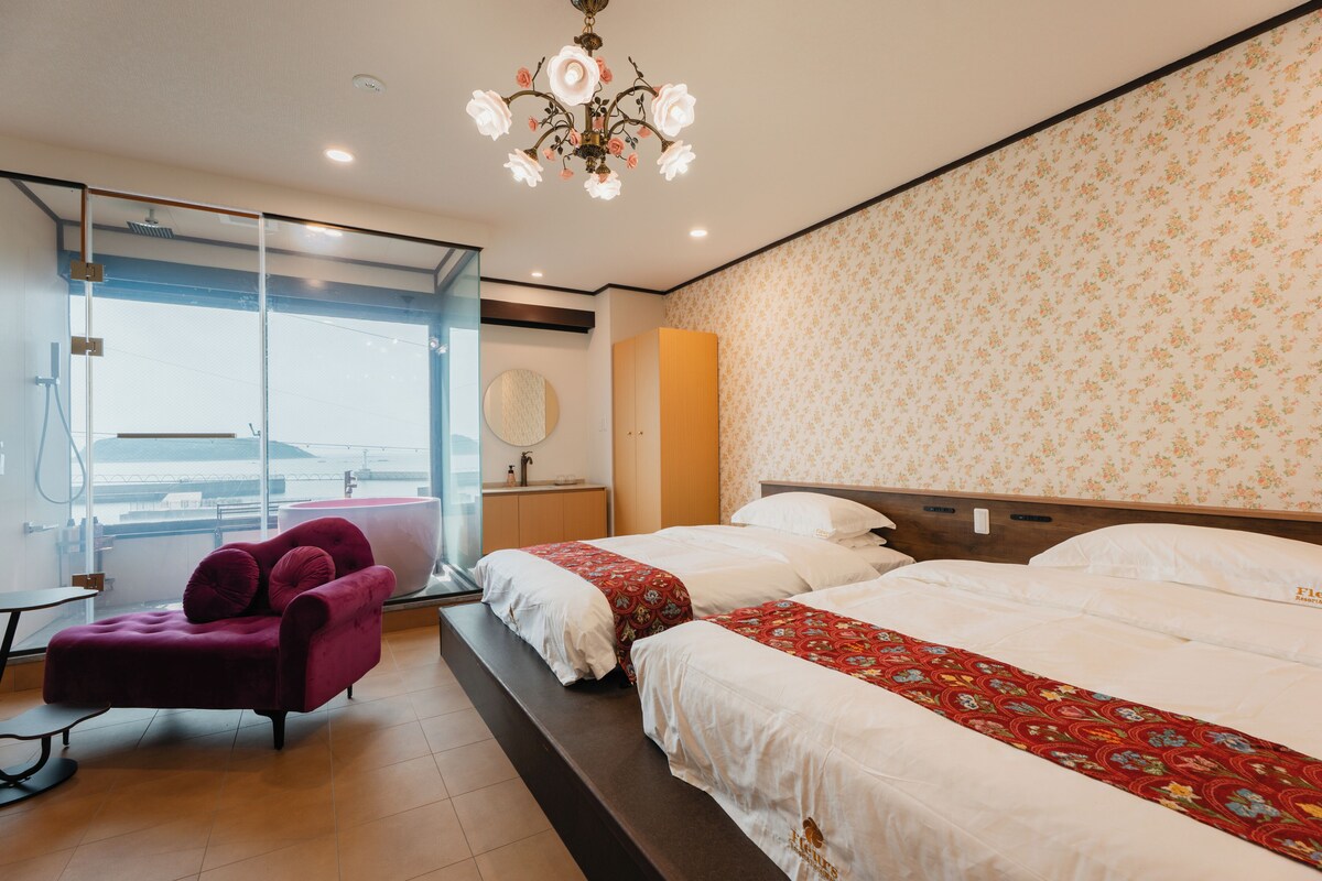 Habitación de hotel con dos camas, un ventanal grande, una silla morada y un candelabro.