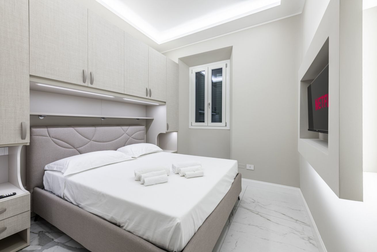 A modern bedroom with a bed, built-in wardrobe, bedside table, and a TV mounted on the wall.