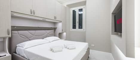 A modern bedroom with a bed, built-in wardrobe, bedside table, and a TV mounted on the wall.
