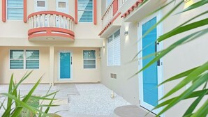 Un edificio de varios pisos con un balcón, una puerta azul y una pequeña zona de jardín con grava.