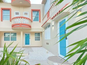 Ein mehrstöckiges Gebäude mit Balkon, blauer Tür und einem kleinen Garten mit Kies.