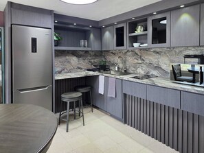 Eine moderne Küche mit integriertem Kühlschrank, einer Marmorarbeitsplatte und einer Bar mit Hockern.