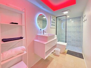 Et moderne badeværelse med vaskebord, rundt spejl, bruser og toilet.