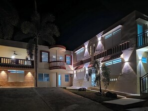 A modern multi-story building with balconies, a covered patio, and a well-lit exterior at night. - Bahía Bonita | Cozy Cabo Rojo Retreat (Cabo Rojo)
