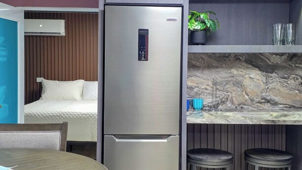 Una kitchenette compacta con refrigerador de acero inoxidable, una pequeña barra con taburetes y una cama en la habitación contigua.
