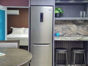 A compact kitchenette with a stainless steel refrigerator, a small bar area with stools, and a bed in the adjacent room. - Bahía Bonita | Cozy Cabo Rojo Retreat (Cabo Rojo)
