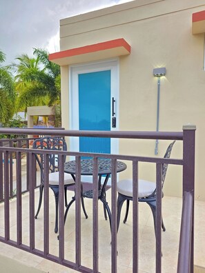 A balcony with a metal railing, a blue door, and two round tables with chairs. - Brisa Del Caribe | Top Floor Studio in Cabo Rojo (Cabo Rojo)