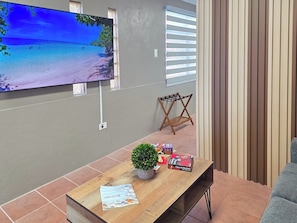 A living room with a flat-screen TV mounted on the wall, a wooden coffee table with a plant, books, and a card. - Brisa Del Caribe | Top Floor Studio in Cabo Rojo (Cabo Rojo)