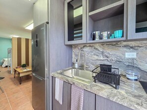 A modern kitchen with a stainless steel refrigerator, a marble countertop, a sink with a faucet, and a black drying rack. - Brisa Del Caribe | Top Floor Studio in Cabo Rojo (Cabo Rojo)