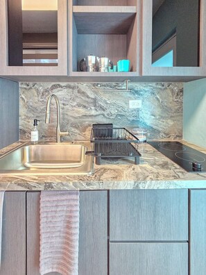 A modern kitchen with a marble backsplash, stainless steel sink, and black stove. - Brisa Del Caribe | Top Floor Studio in Cabo Rojo (Cabo Rojo)