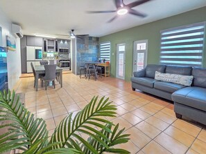 Ein Wohnzimmer mit Sofa, eine Essecke mit Stühlen, eine Küche mit Schränken und einem Deckenventilator.
