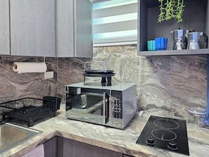 A modern kitchen with a built-in microwave, a black induction cooktop, and a stainless steel sink. - Palmera Azul | Cozy Private Apartment in Cabo Rojo (Cabo Rojo)