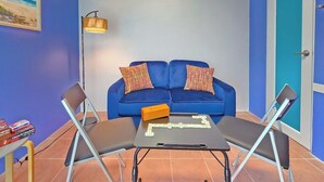 A room with a blue sofa, two chairs, a table with dominoes, a lamp, and a door. - Palmera Azul | Cozy Private Apartment in Cabo Rojo (Cabo Rojo)
