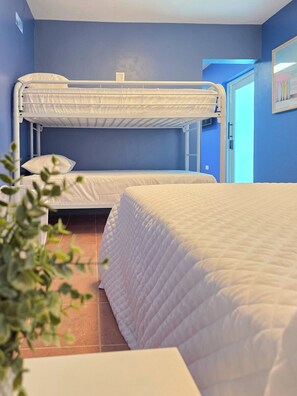 A room with bunk beds and a single bed, blue walls, and a visible door. - Palmera Azul | Cozy Private Apartment in Cabo Rojo (Cabo Rojo)