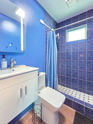 Een badkamer met een blauwe wand, een wit wastafelmeubel, een toilet en een douchegordijn.