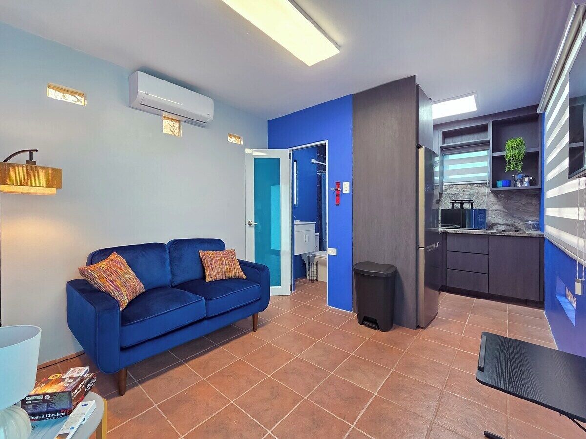 A compact living space with a blue sofa, a kitchen area, and a visible bathroom.