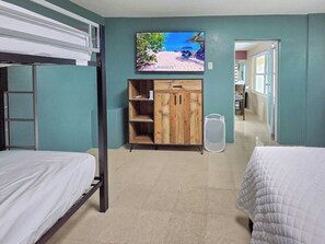 A room with bunk beds, a wooden cabinet, a television, and a trash bin. - Villa Andrea | Cabo Rojo Private Estate (Cabo Rojo)