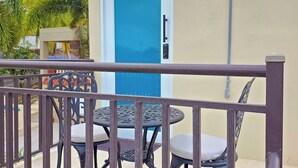 Ein Balkon mit Metallgeländer, einer blauen Tür und zwei runden Tischen mit Stühlen.