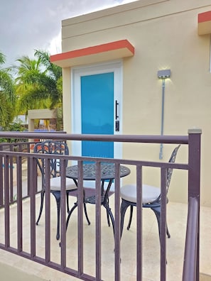 Ein Balkon mit Metallgeländer, einer blauen Tür und zwei runden Tischen mit Stühlen.