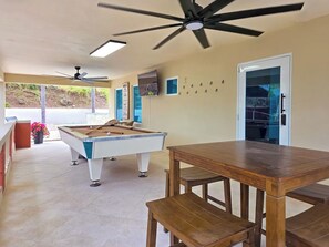 A pool table with a ceiling fan, a wooden table, and a bench in a room with a door and a window. - Villa Andrea | Cabo Rojo Private Estate (Cabo Rojo)