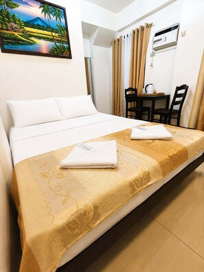 A hotel room with a bed, a desk, a chair, and a painting on the wall. - Metrohive Apartment 2D - Cozy Studio Near Airport & PITX (Pasay City)