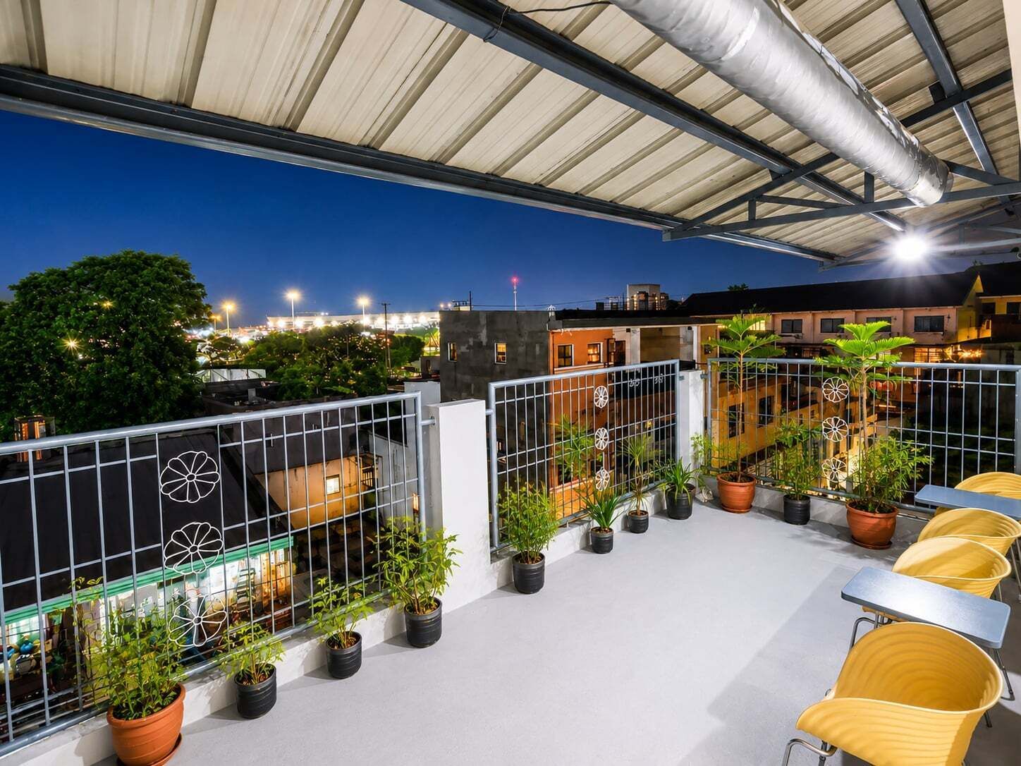 A rooftop terrace with potted plants, outdoor seating, and a view of the cityscape at dusk.