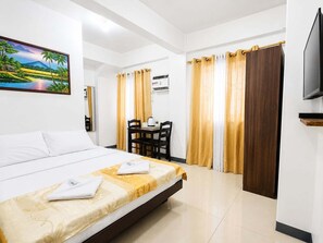 A hotel room with a bed, a desk with a chair, a television, and a painting on the wall. - Metrohive Apartment 2D - Cozy Studio Near Airport & PITX (Pasay City)