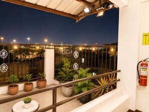 Ein Balkon mit Topfpflanzen, einem Feuerlöscher und Blick auf die beleuchtete Stadt.