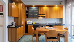 Cocina compacta con armarios de madera, encimera negra, microondas, hervidor y una mesa de comedor con sillas.