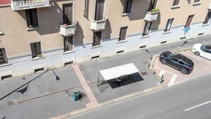 Vista de la calle con un refugio de autobús cubierto, un coche aparcado y un edificio con balcones.