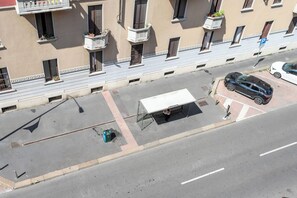 Straßenansicht mit überdachter Bushaltestelle, einem parkenden Auto und einem Gebäude mit Balkonen.