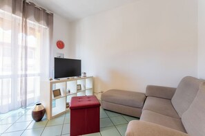 A living room with a flat-screen TV on a white stand, a red ottoman, a beige sofa, and a large window with sheer curtains. - Apartment in Milan with 1 bedrooms sleeps 2 (Milan)