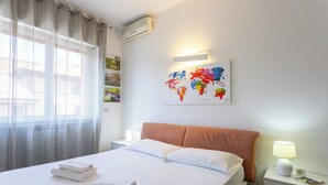 Habitación de hotel con cama, mesita de noche, lámpara y un cuadro con un mapa mundial en la pared.