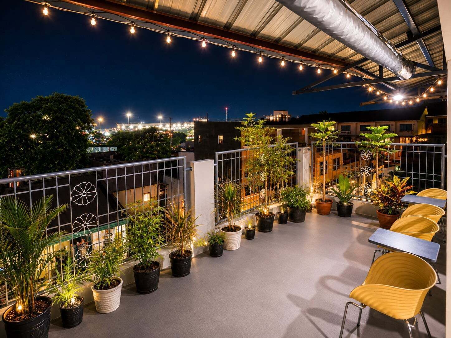 A rooftop terrace with potted plants, outdoor seating, and string lights.
