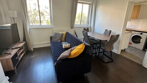 Ein kompakter Wohnbereich mit Sofa, Fernseher, Esstisch, Stühlen und Waschmaschine.