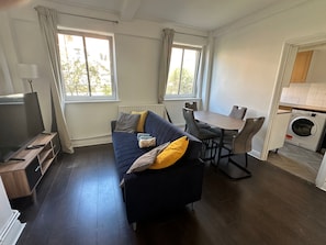 Ein kompakter Wohnbereich mit Sofa, Fernseher, Esstisch, Stühlen und Waschmaschine.
