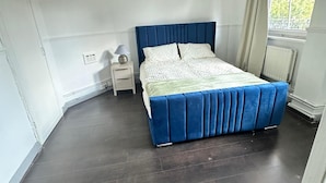 Ein Schlafzimmer mit einem Bett, einem Nachttisch, einer Lampe und einem Fenster mit Vorhängen.
