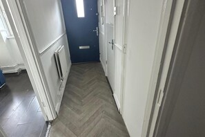 Un pasillo estrecho con suelo de espiga, un radiador y una puerta con pomo.