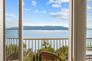 Ein Balkon mit Blick auf ein ruhiges Gewässer und sanfte Hügel in der Ferne.