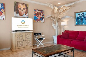 Un salon avec un canapé rouge, une table basse, un téléviseur diffusant l’émission « GRAND WELCOME BRANSON & THE OZARKS », et des œuvres d’art mural.